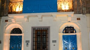 A building with two blue doors, a window with a metal grill, and a sign above the right door.
