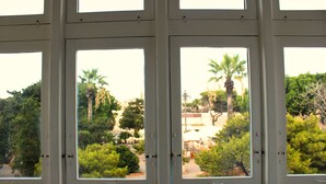 A view through a window with multiple panes, revealing a courtyard with palm trees and greenery.