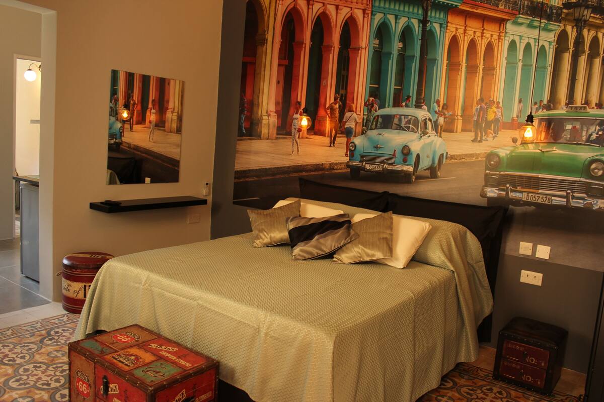 A hotel room with a bed, a painting of a street scene, and vintage suitcases.