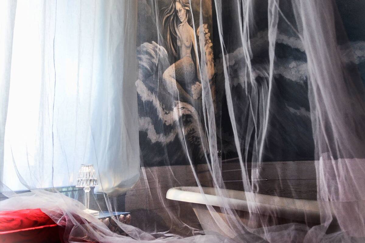 Un lit avec une couvre-lit rouge, un rideau blanc et une moustiquaire.