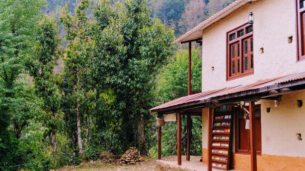A rustic building with a tiled roof and wooden beams, surrounded by lush greenery and trees.
