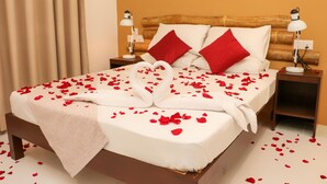 Cama bem arrumada com pétalas de rosa e arranjo de toalha em forma de cisne, duas luminárias de cabeceira e cabeceira de madeira.