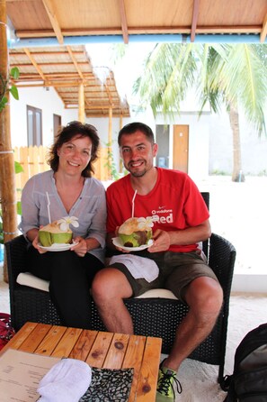 Two people seated on a wicker chair outdoors, holding plates with food. - The Castaway Retreat (Feridhoo)