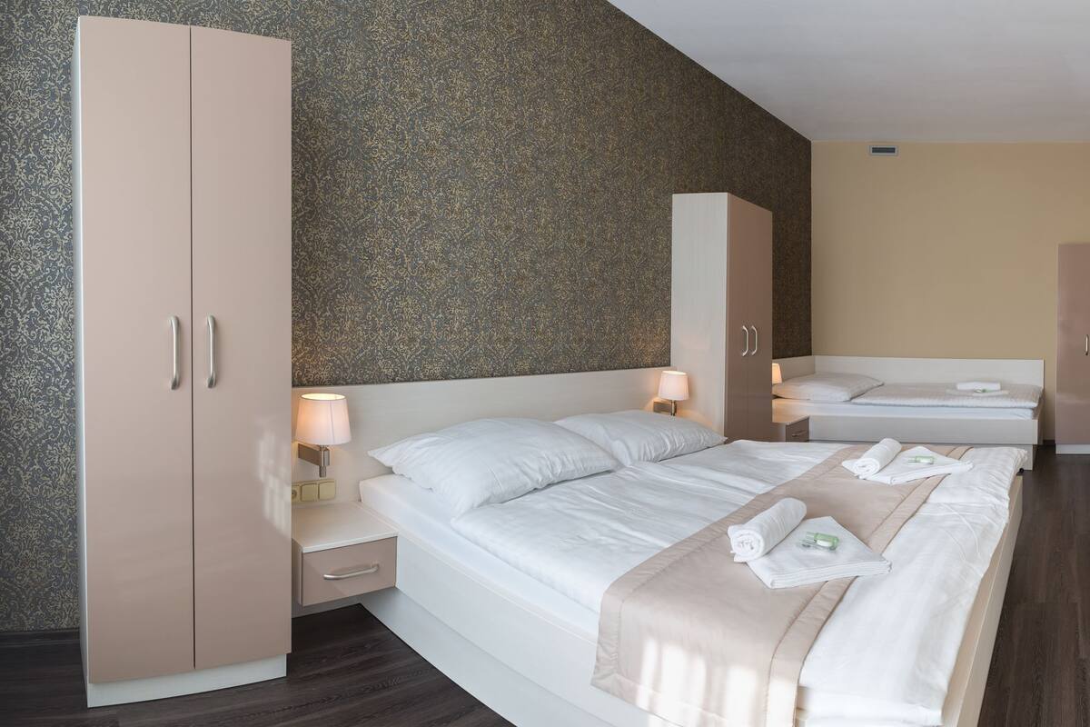A hotel room with a bed, a wardrobe, a TV, and a nightstand with a lamp.