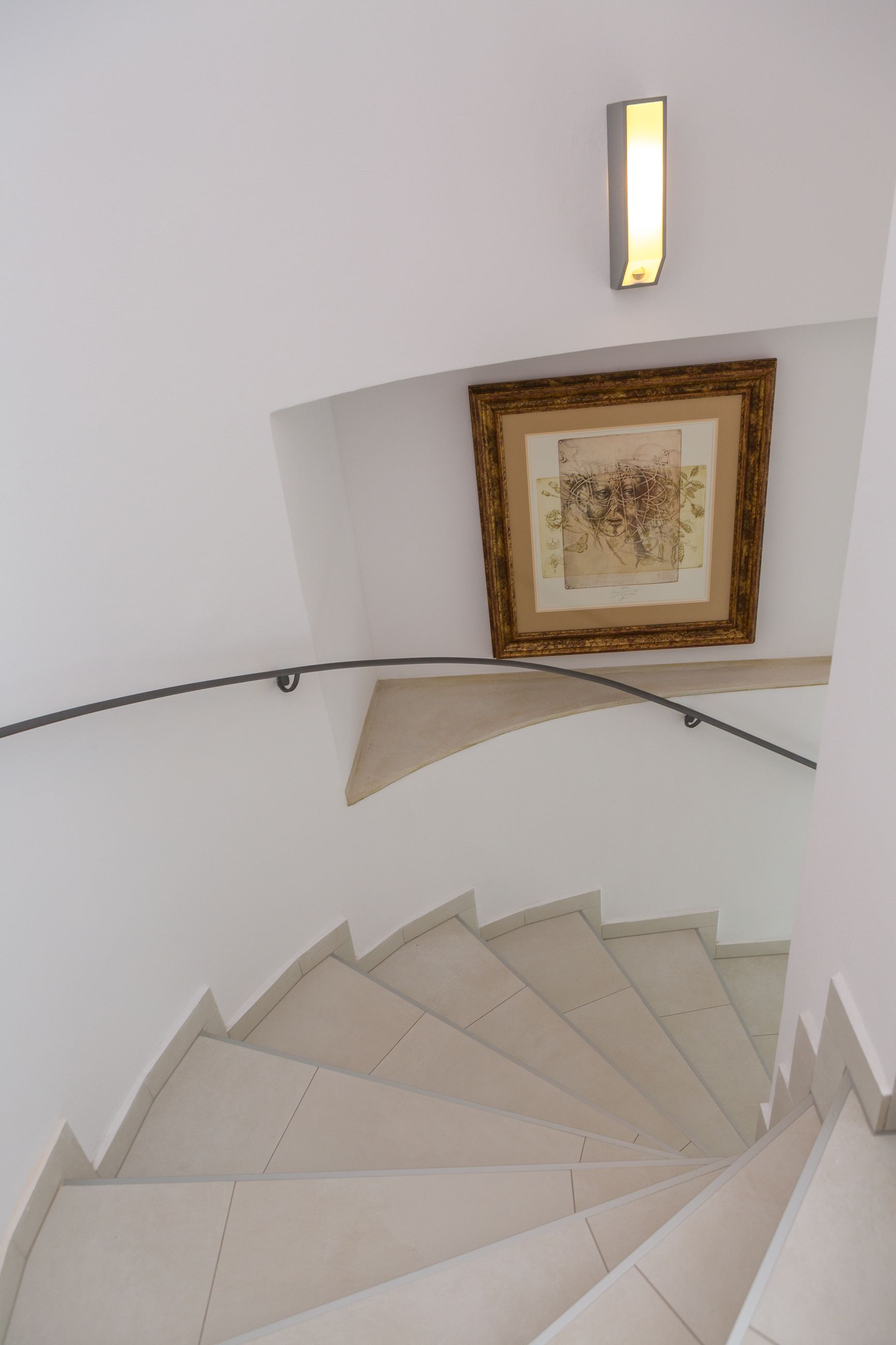 A spiral staircase with a handrail and a framed artwork above it.