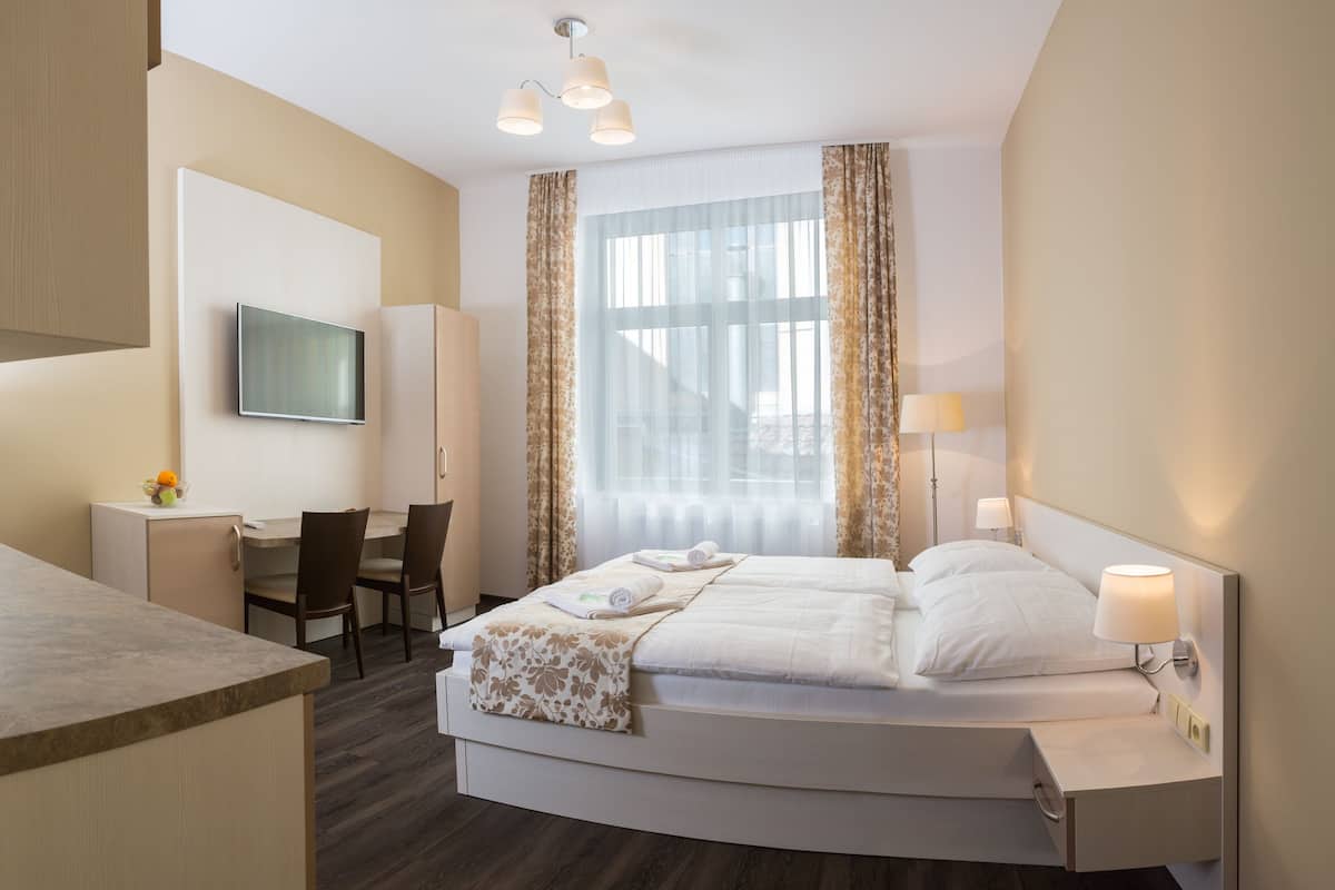A hotel room with a bed, bedside tables, a desk, and a television.
