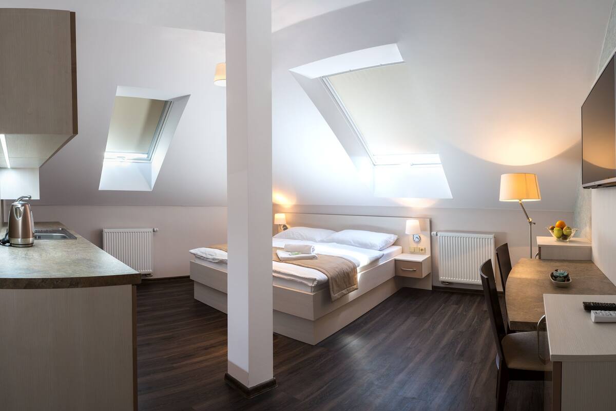 A modern hotel room with a skylight, a bed, a desk, and a chair.