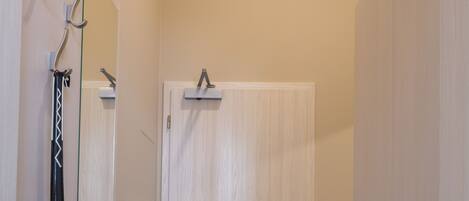 A hallway with a wooden floor, a white door with a handle, and a mirror on the left wall.