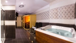 A modern bathroom with a large bathtub, a glass shower enclosure, and a wooden sauna door. - Penzion Longus (Kyjov)
