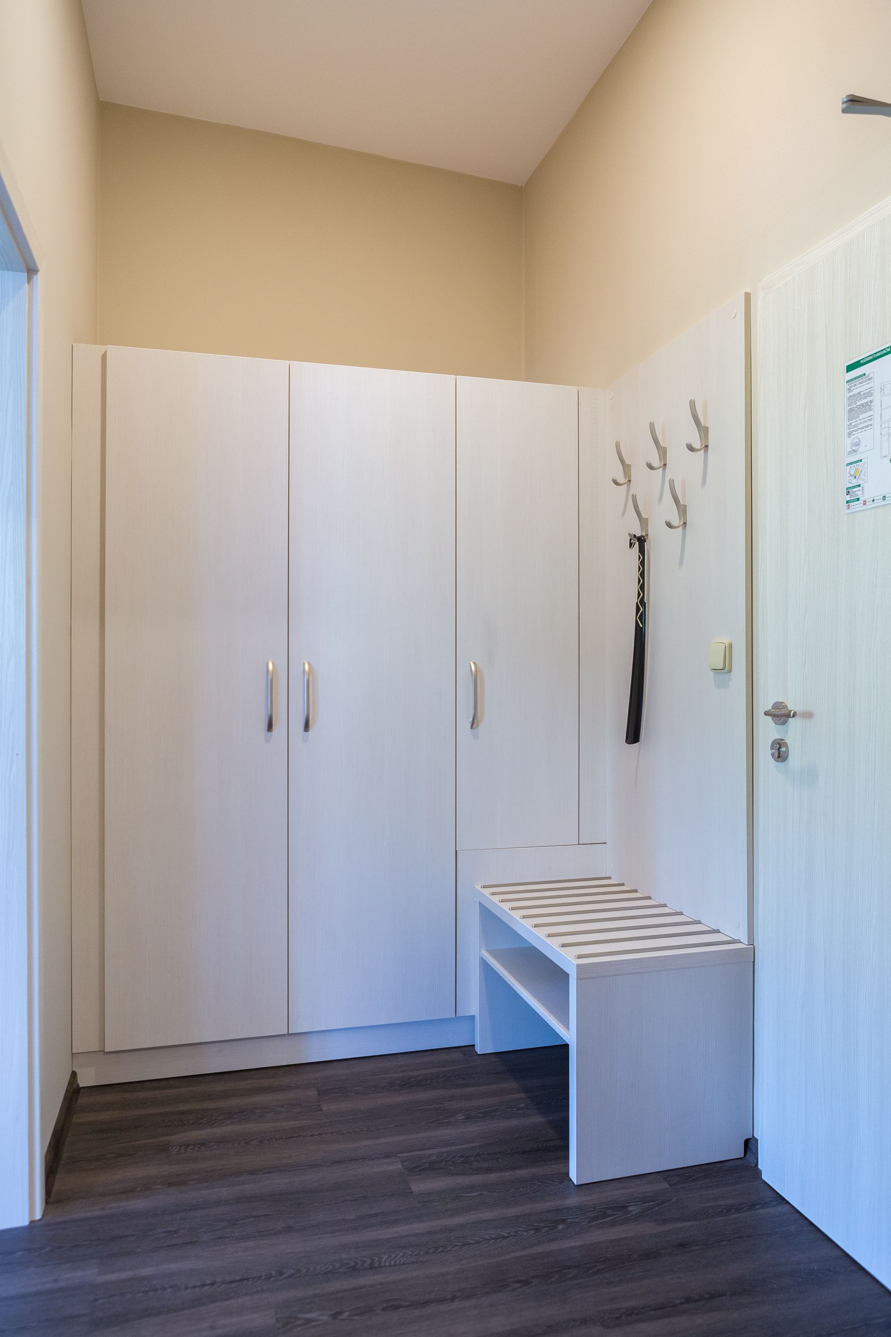 A hallway with a white wardrobe, a bench, and a door with a coat hanging on it.