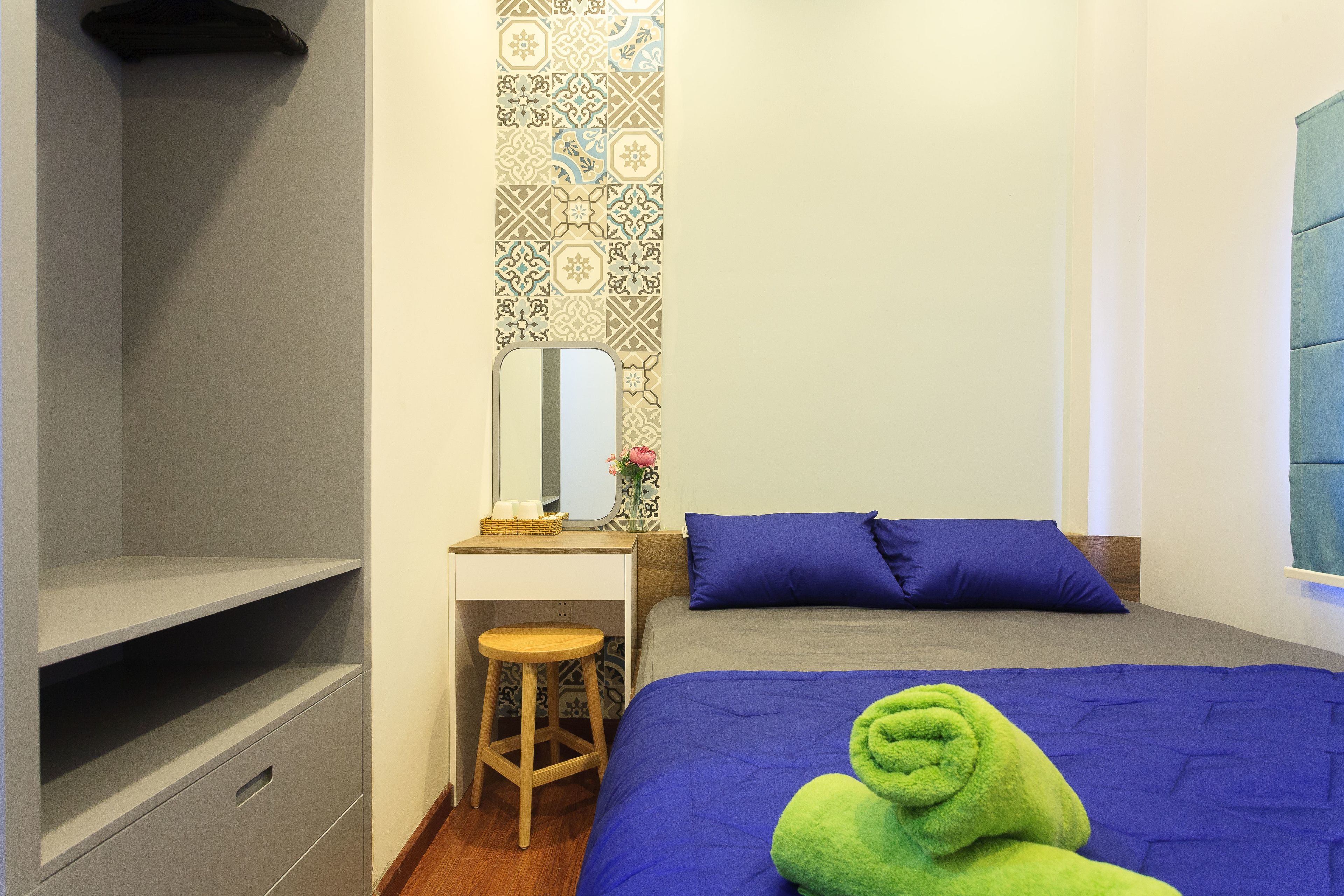 A bedroom with a bed, a desk, a chair, a mirror, and a patterned wall.