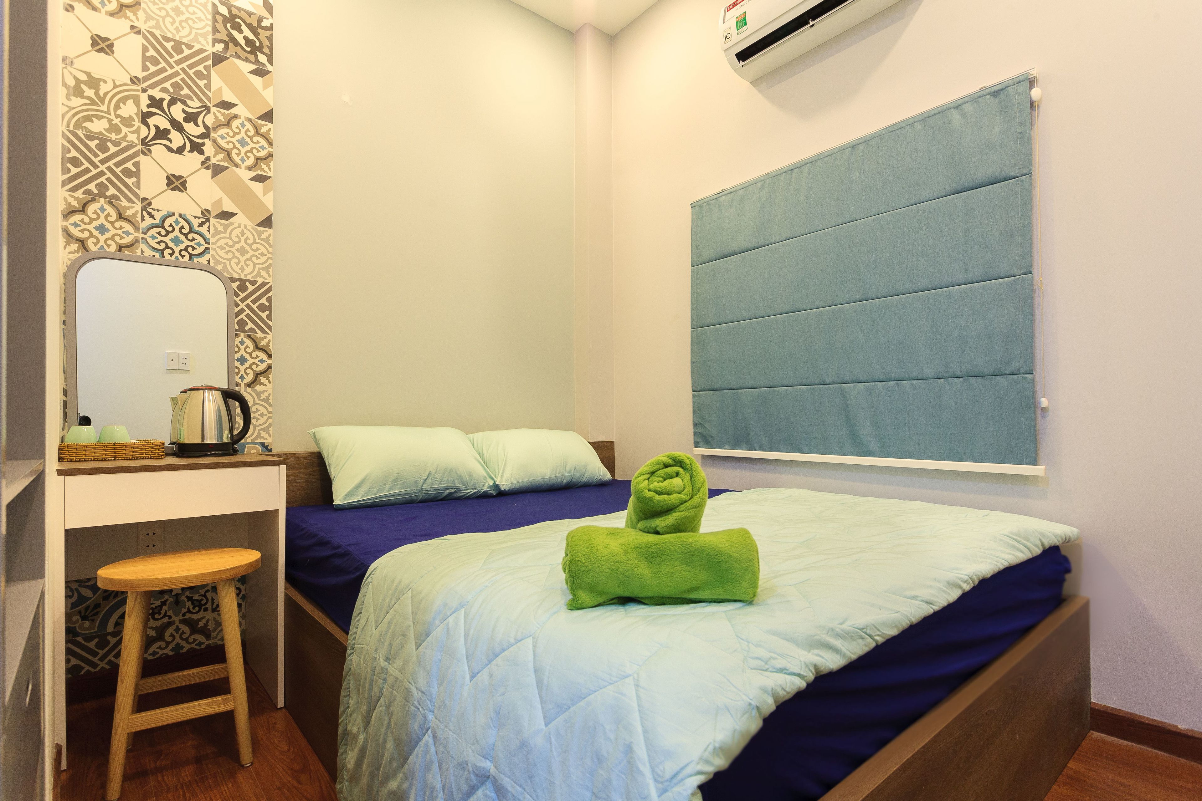 A small, neatly arranged bedroom with a bed, a desk, and a stool.