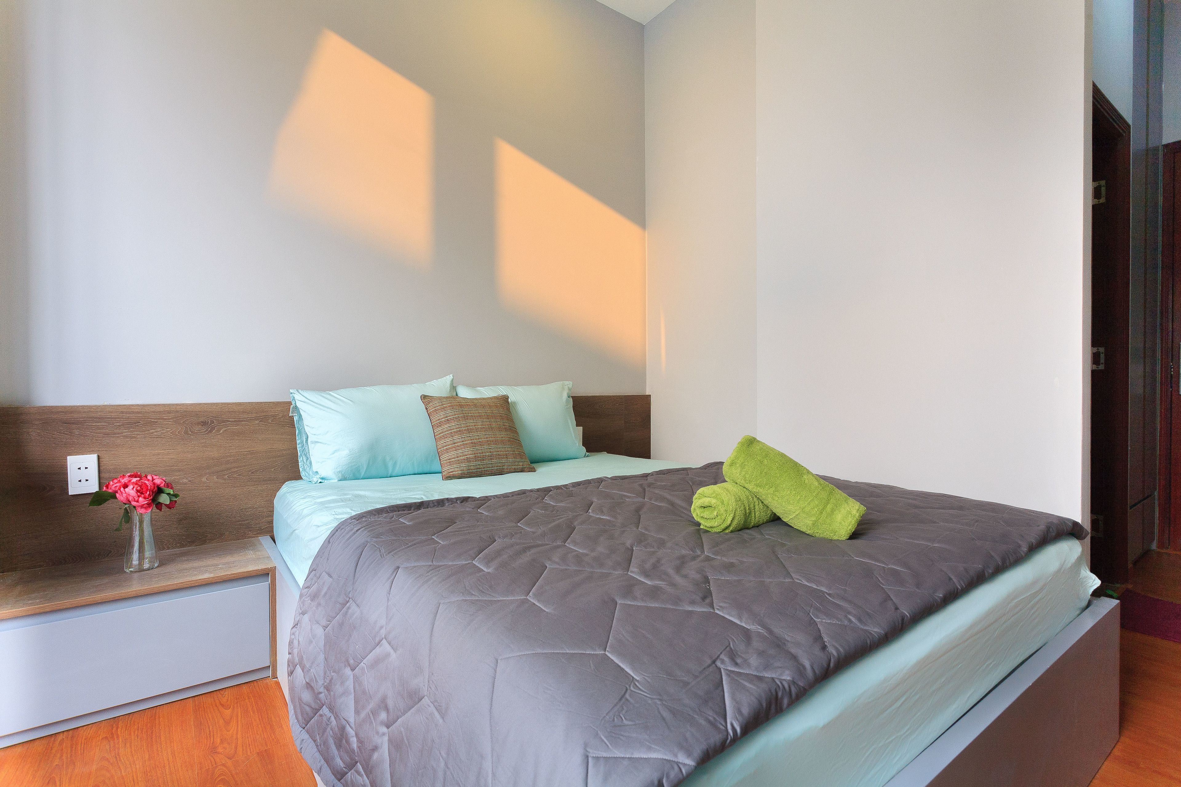 A neatly made bed with a grey quilt, a green towel, and two pillows on a wooden headboard.