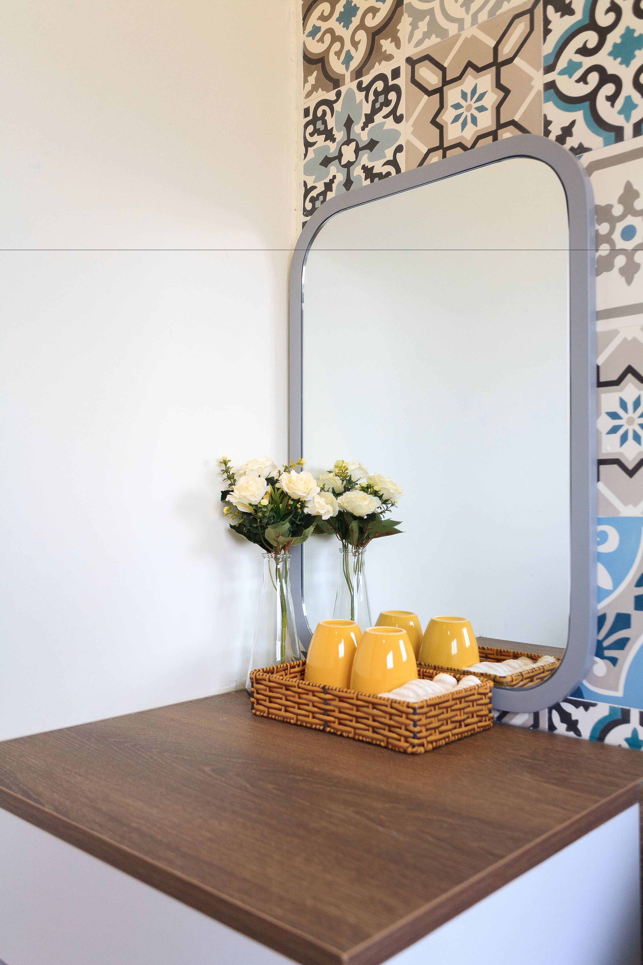 Une coiffeuse en bois avec un miroir, un vase de fleurs blanches et un panier de bougies jaunes.