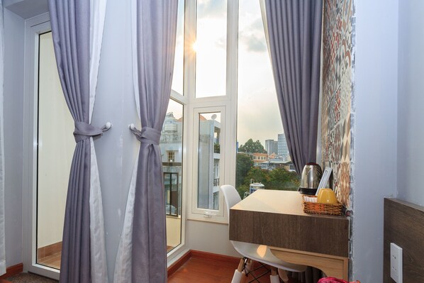 A room with a view of a cityscape through a large window, a table with a basket, and a chair.