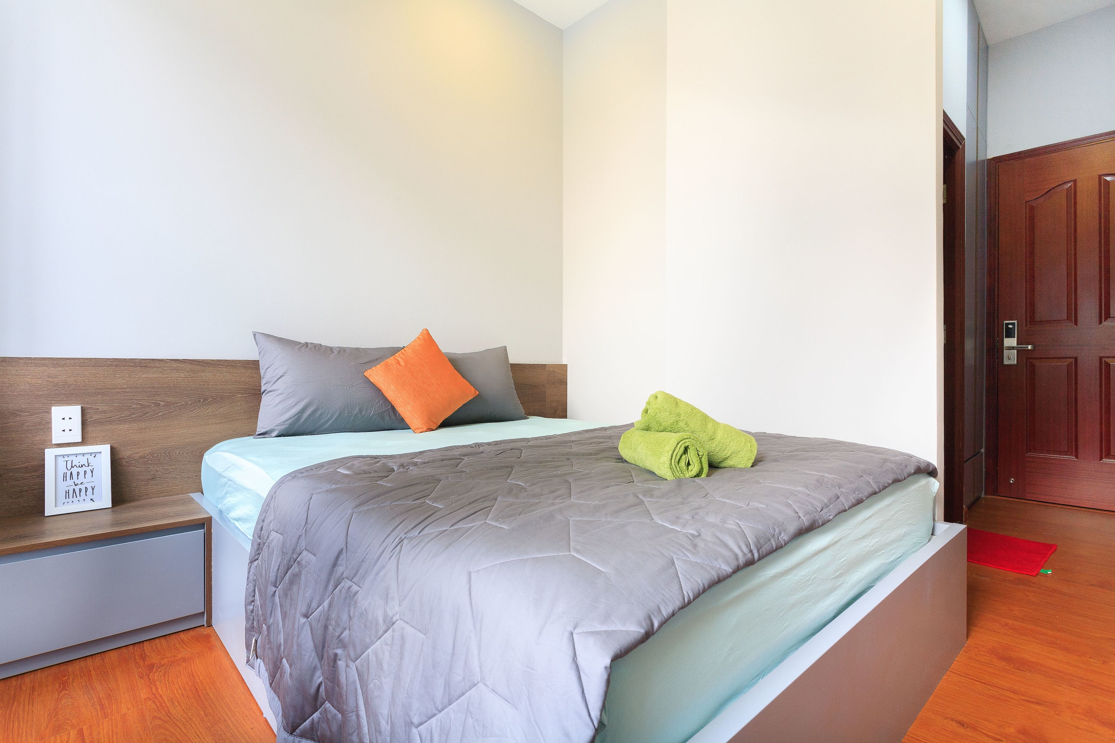 A neatly made bed with a grey quilt, a wooden headboard, and a small bedside table with a sign.