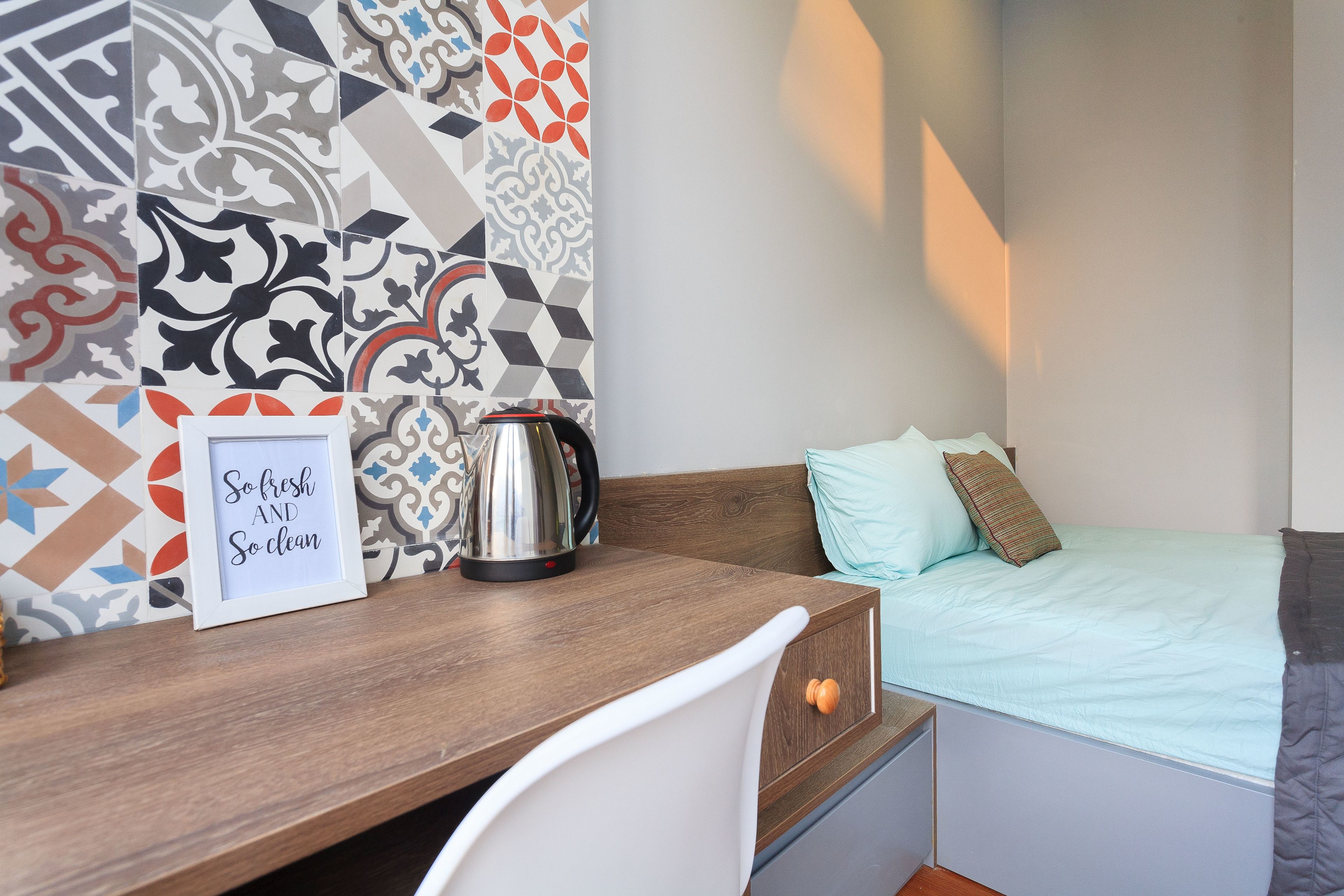 A compact room with a bed, a desk, and a kettle.