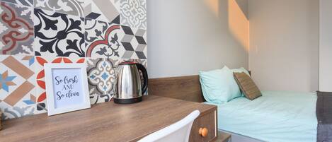 A compact room with a bed, a desk, and a kettle.