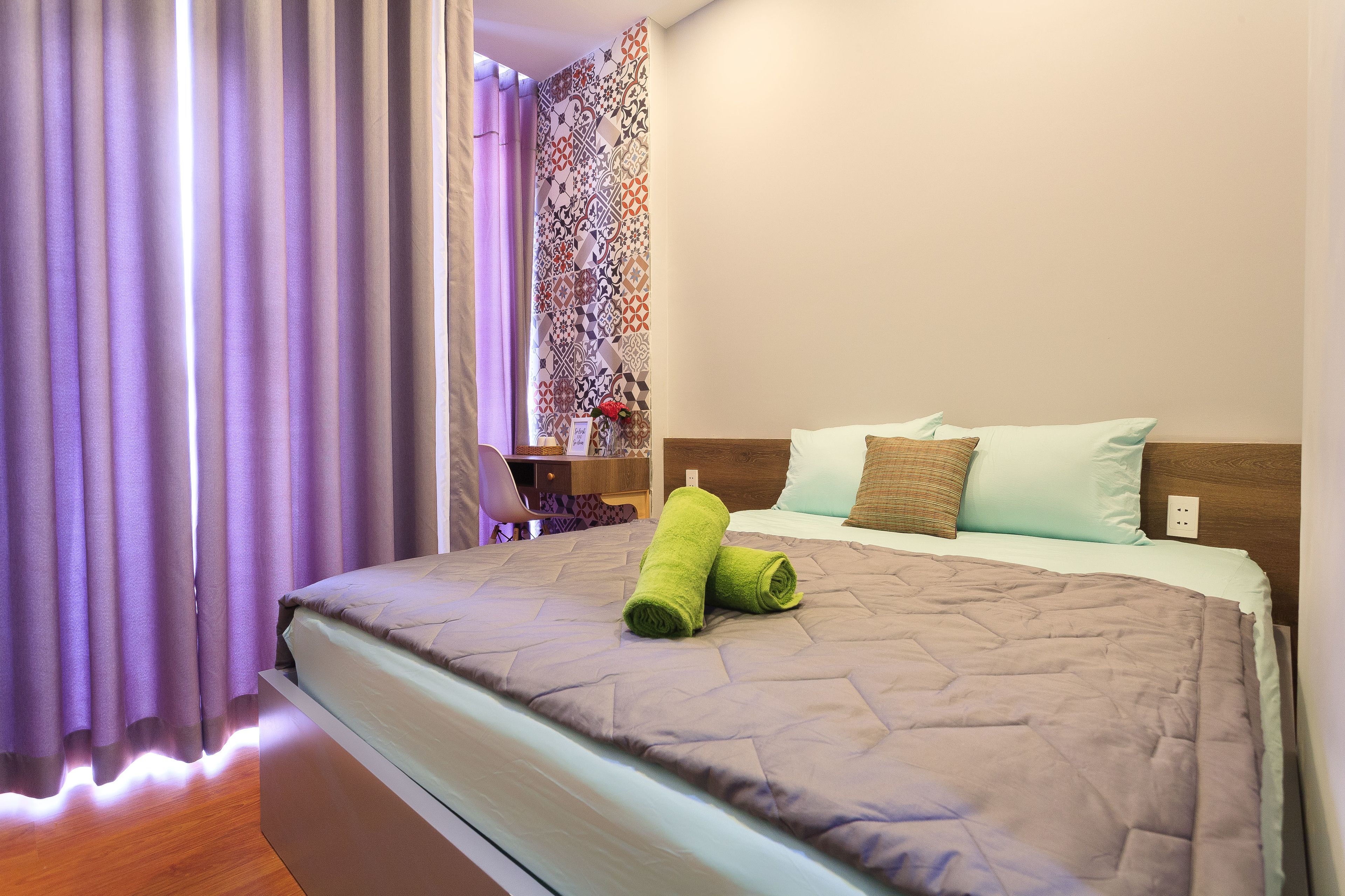 A neatly made bed with a brown quilt, a green towel, and two pillows.
