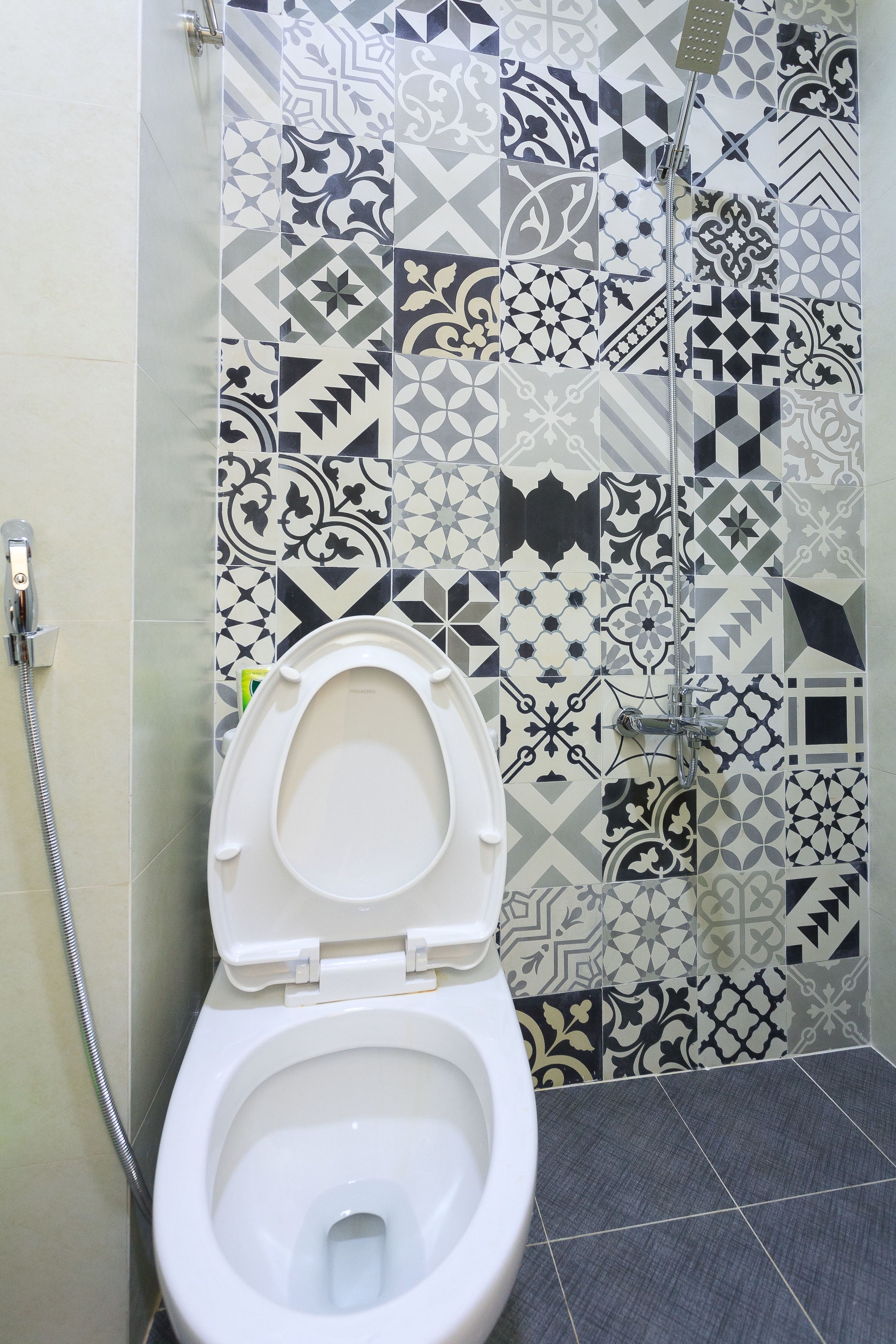 Un baño con inodoro, ducha y baldosas estampadas.