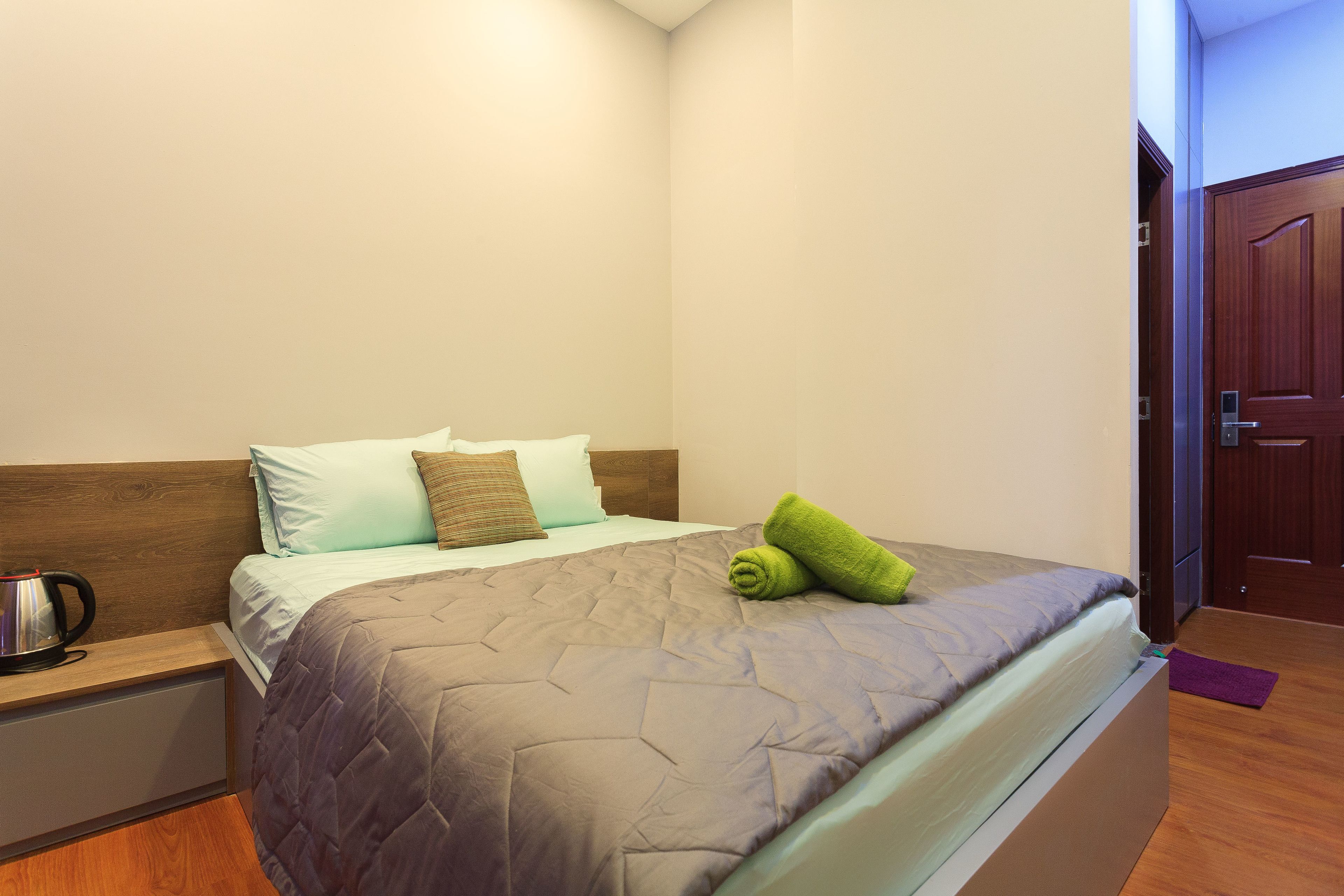 Una cama bien hecha con un cabecero acolchado, una almohada y una toalla enrollada.