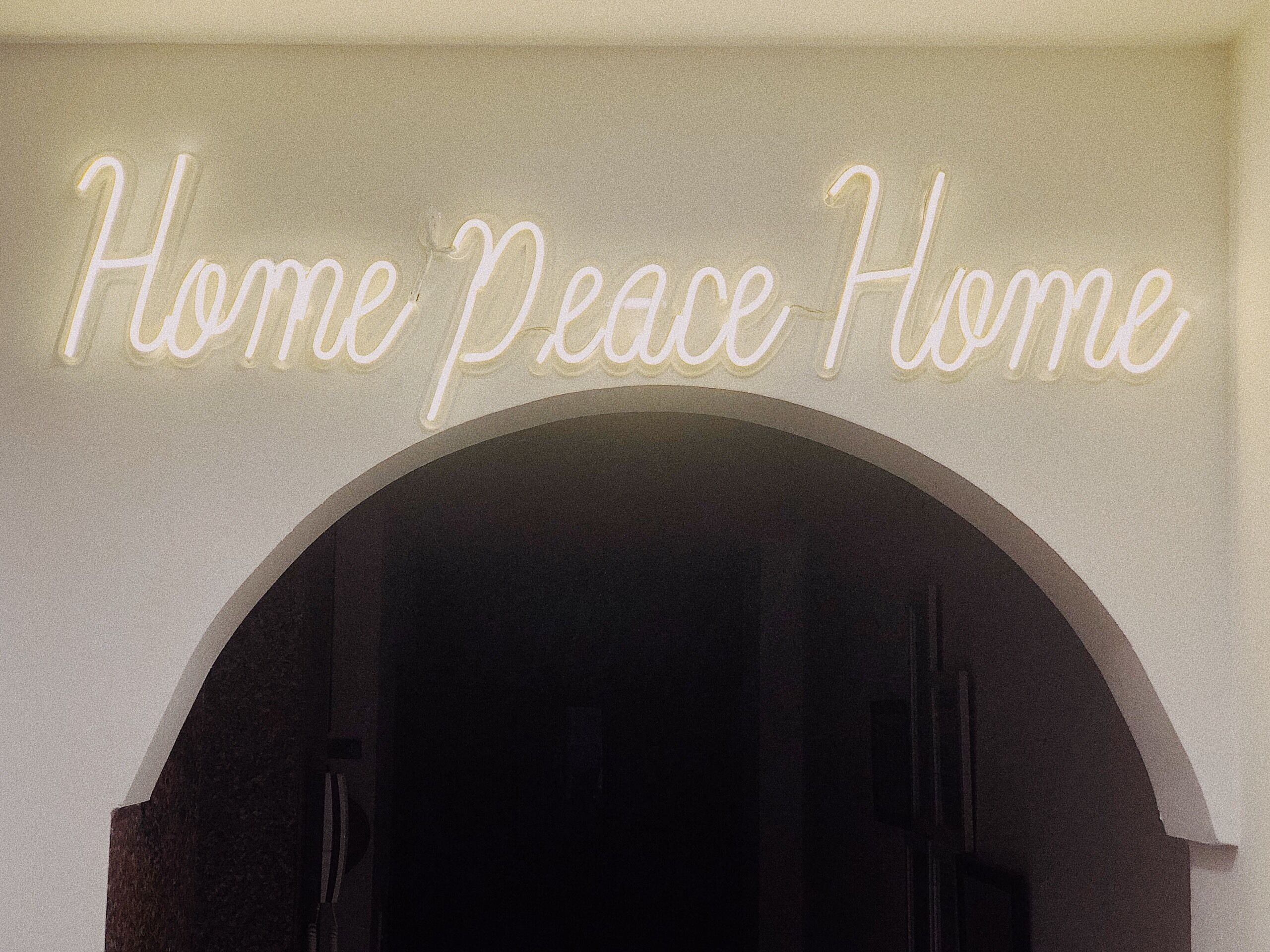A neon sign above an arched doorway with the text "Home Peace Home".