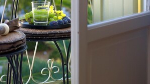 A balcony with a wicker table, a glass of water, and a plate of grapes.