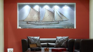 A modern living room with a red accent wall, a large framed artwork of a sailing ship, a leather sofa, and a coffee table.