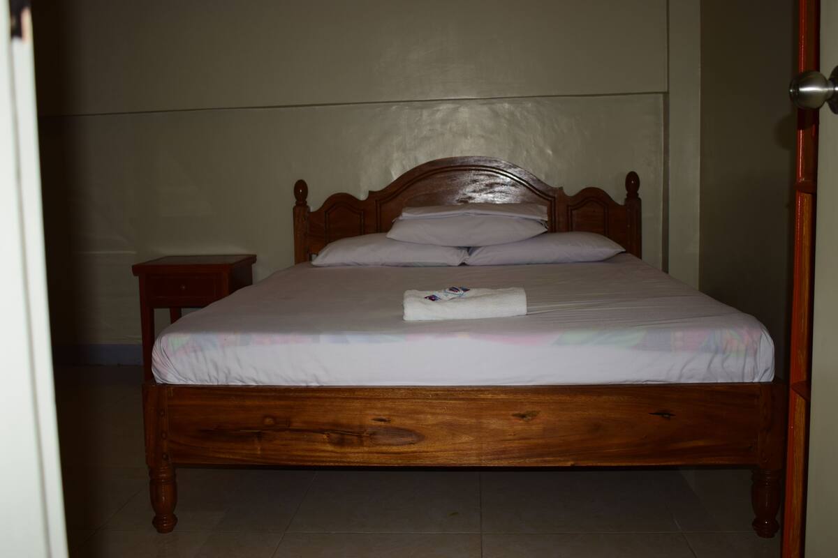 Una cama de madera con cabecera, una mesita de noche y una toalla doblada sobre la cama.