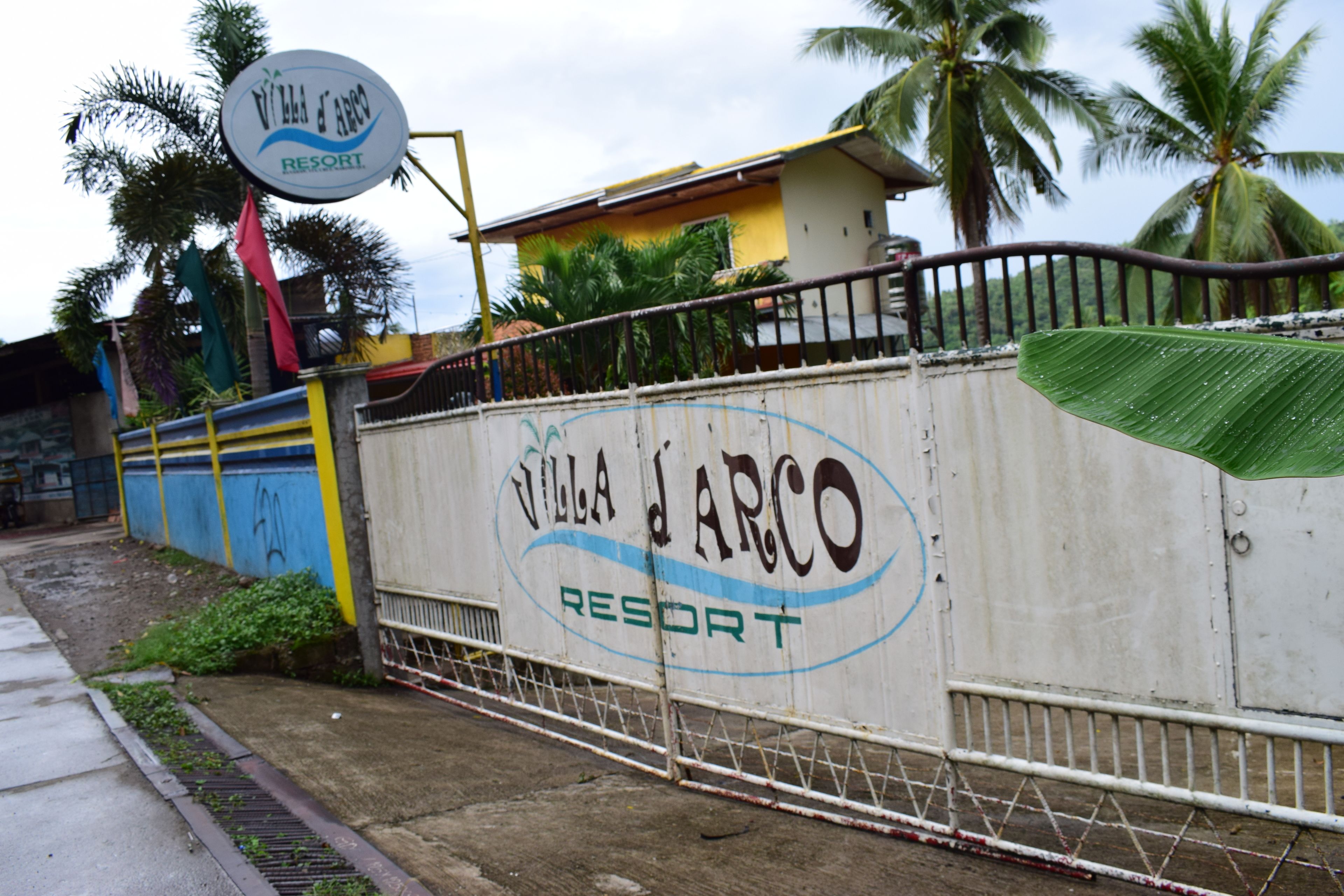A sign for Villa Arco Resort with a gated entrance and palm trees in the background.