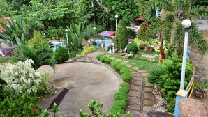 A lush garden with a variety of plants, a paved area, and a small building with a red roof. - Villa d' Arco Resort (Santa Cruz)
