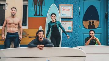 Un grupo de personas con tablas de surf frente a un edificio con una puerta azul y un letrero que dice 'LA VENTANA AZUL'.