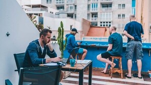 Un grupo de personas en un ambiente exterior informal, con una mesa, sillas, una planta de cactus y una pared azul.