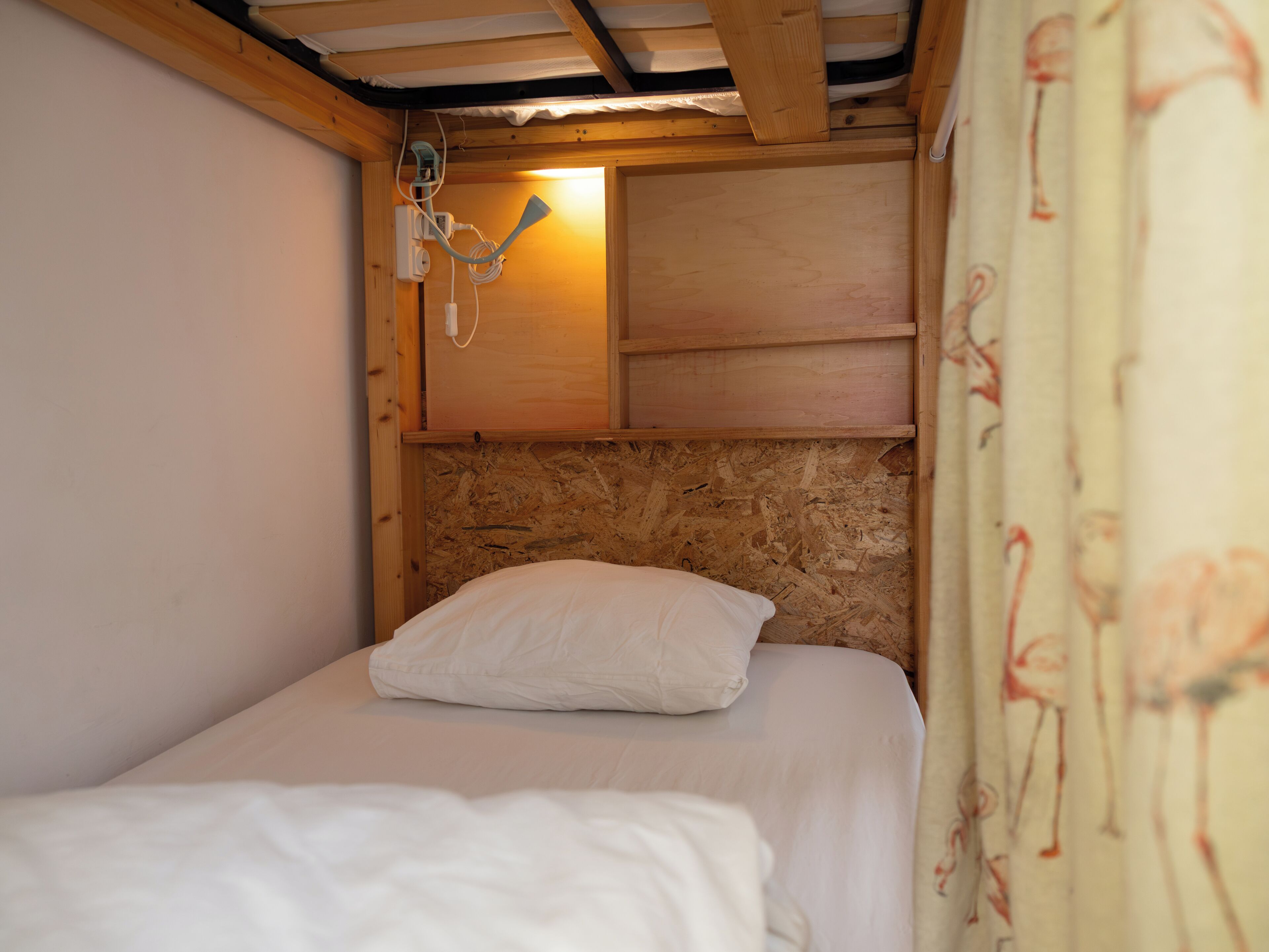 Ein Einzelbett mit hölzernem Kopfteil und einem weißen Kissen in einem rustikalen Zimmer mit sichtbaren Holzbalken und schräg versetzter Decke.