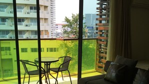 A modern living room with a sofa, a small table, and a balcony with a view of buildings and greenery. - Rocco Hua Hin 512 Condominium (Hua Hin)