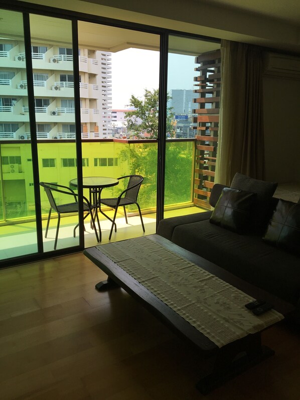A modern living room with a sofa, a small table, and a balcony with a view of buildings and greenery. - Rocco Hua Hin 512 Condominium (Hua Hin)