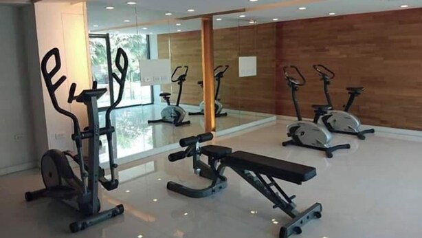 A gym with various exercise equipment, including treadmills and weight machines, in a modern room with large windows and a wooden wall. - Rocco Hua Hin 512 Condominium (Hua Hin)