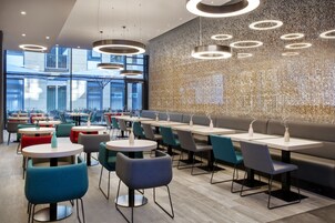 Un restaurante moderno con mesas redondas, sillas coloridas y un muro con estampado.