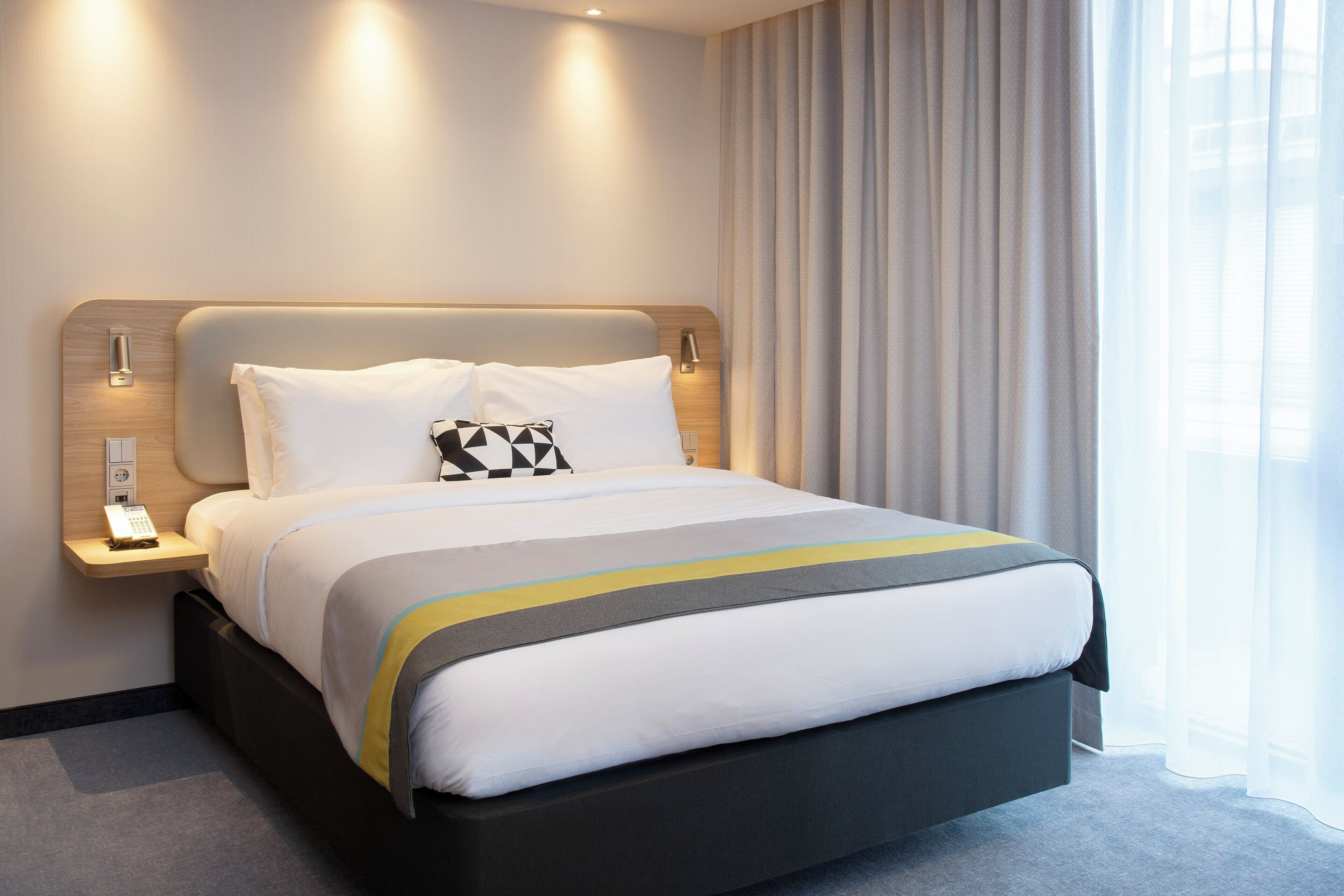 Ein Hotelzimmer mit einem Bett, Nachttischen, einem Telefon und einem Fenster mit Vorhängen.