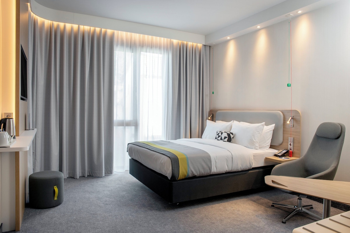 Une chambre d’hôtel moderne équipée d’un lit, d’un bureau, d’une chaise et d’une petite poubelle.