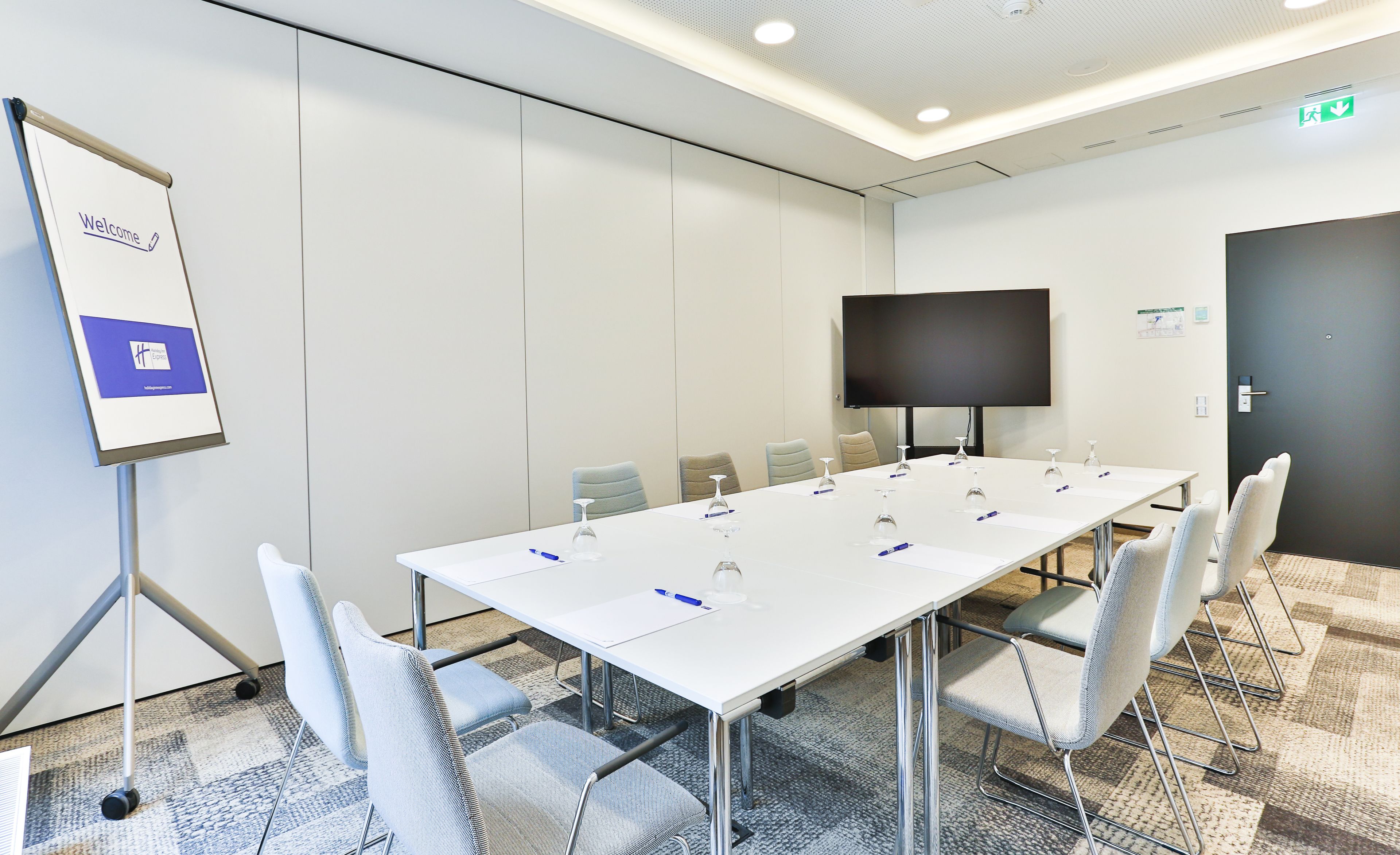 A conference room with a long table, chairs, a whiteboard, and a flat-screen TV.