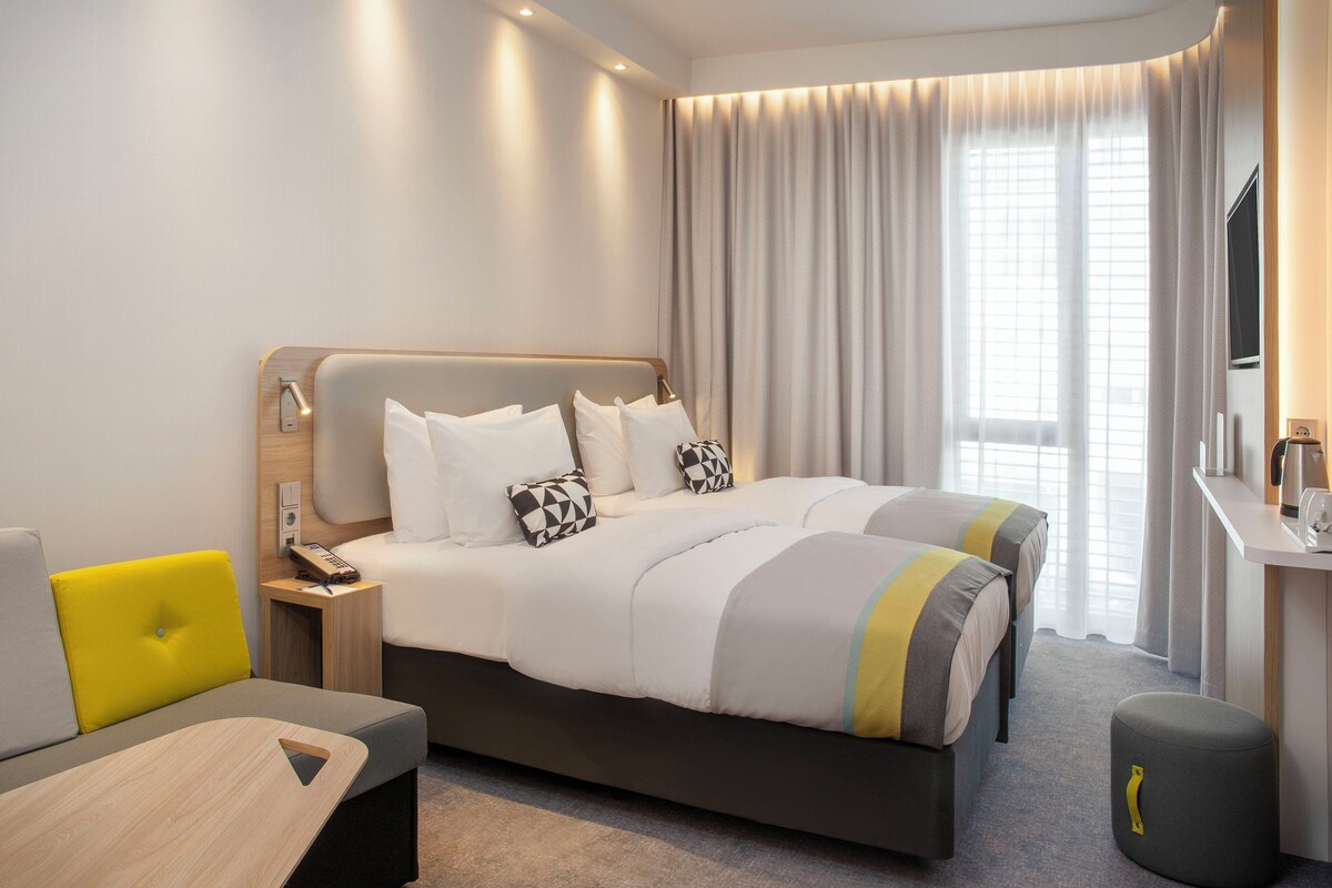 Une chambre d’hôtel comprenant un lit, une table de chevet, une lampe et un bureau avec une chaise.