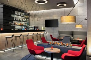 A modern bar area with a long counter, multiple stools, and a seating area with round tables and red chairs.