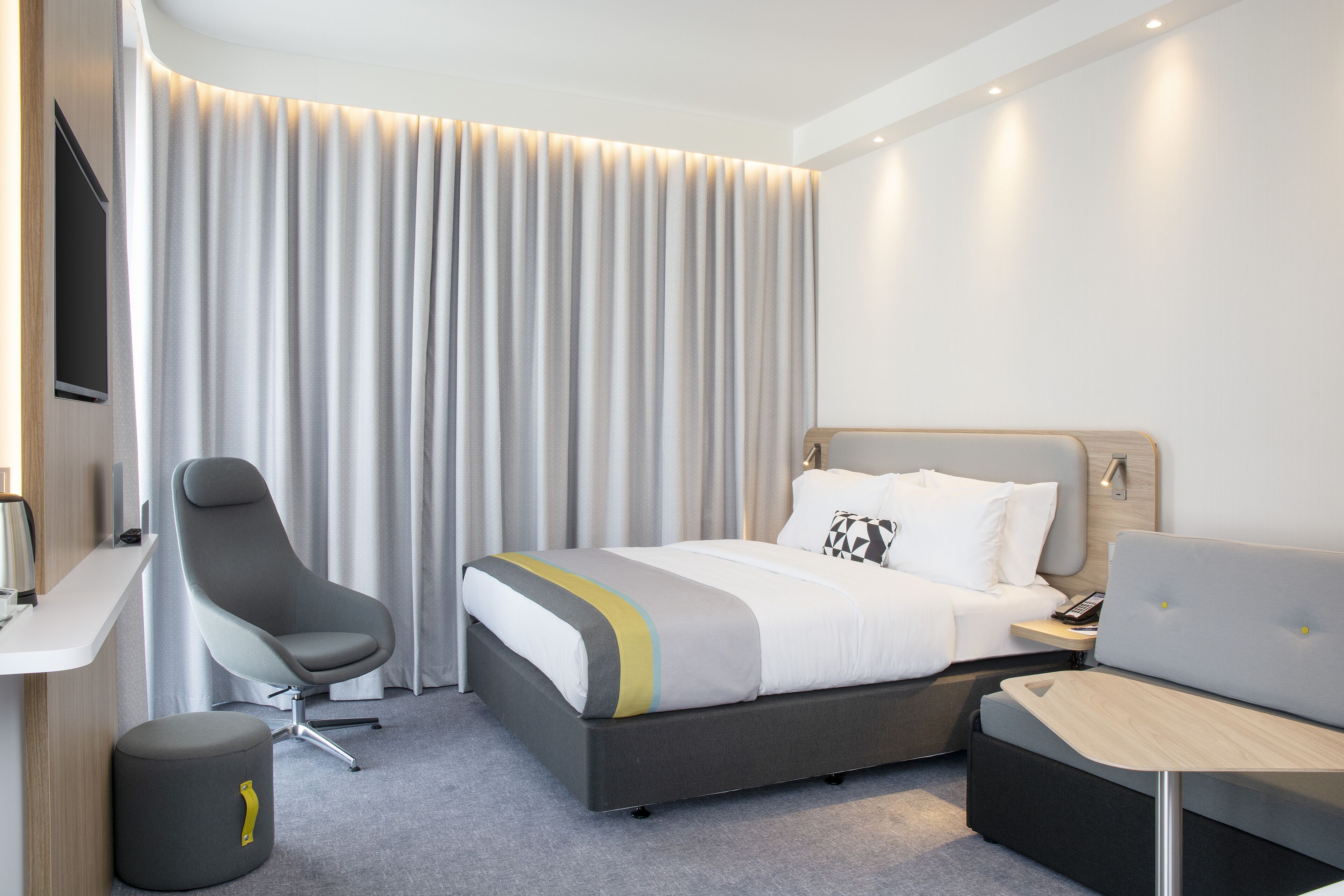 A modern hotel room with a bed, a desk, a chair, and a sofa.