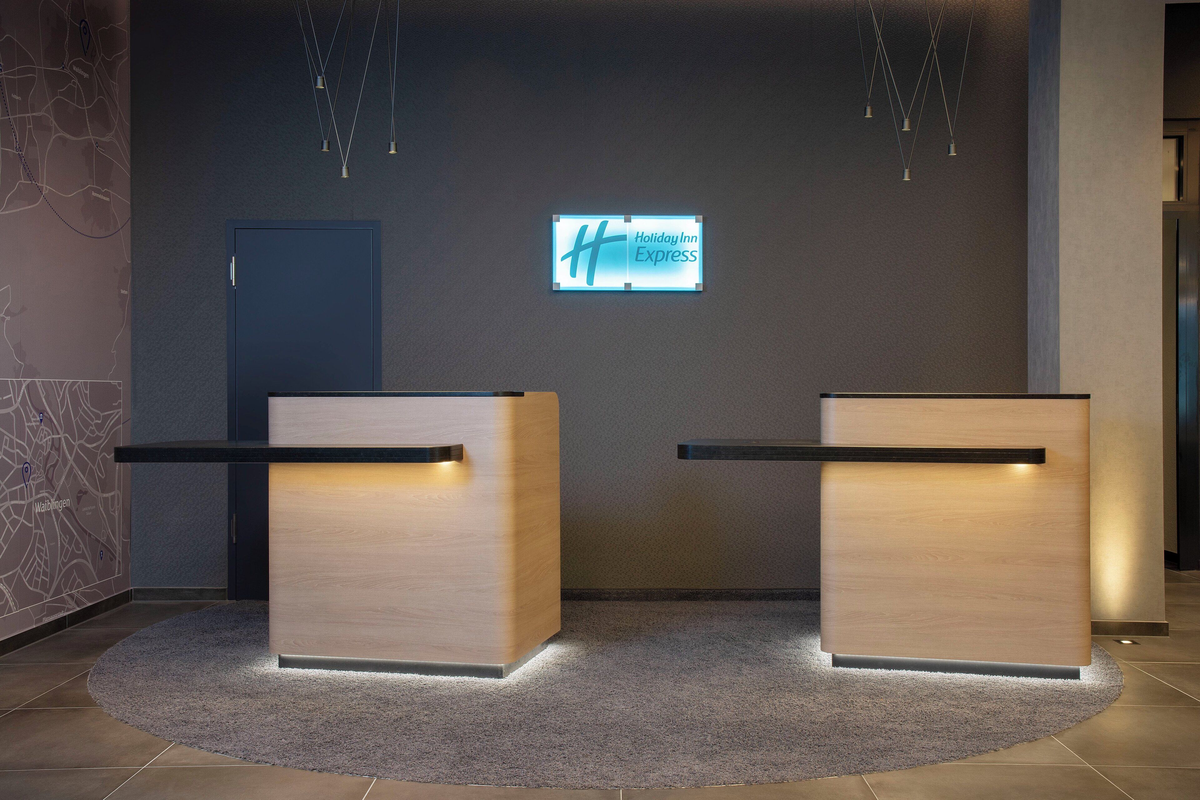 Ein Empfangsbereich mit einem digitalen Schild, das 'Holiday Inn Express' anzeigt, und einer dunklen Tür im Hintergrund.