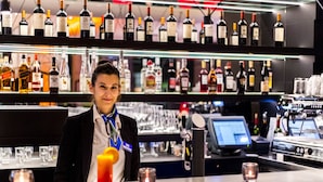 Zona de bar con estantes llenos de botellas de licores, una barra y un terminal de pago digital.