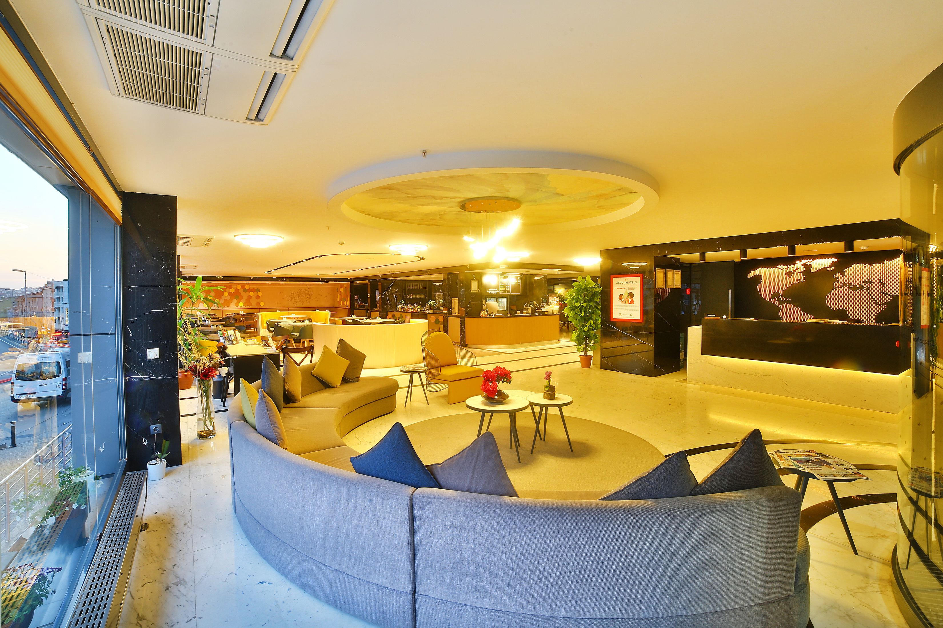 A modern hotel lobby with a curved seating area, a reception desk, and a large digital world map display.