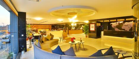 A modern hotel lobby with a curved seating area, a reception desk, and a large digital world map display.
