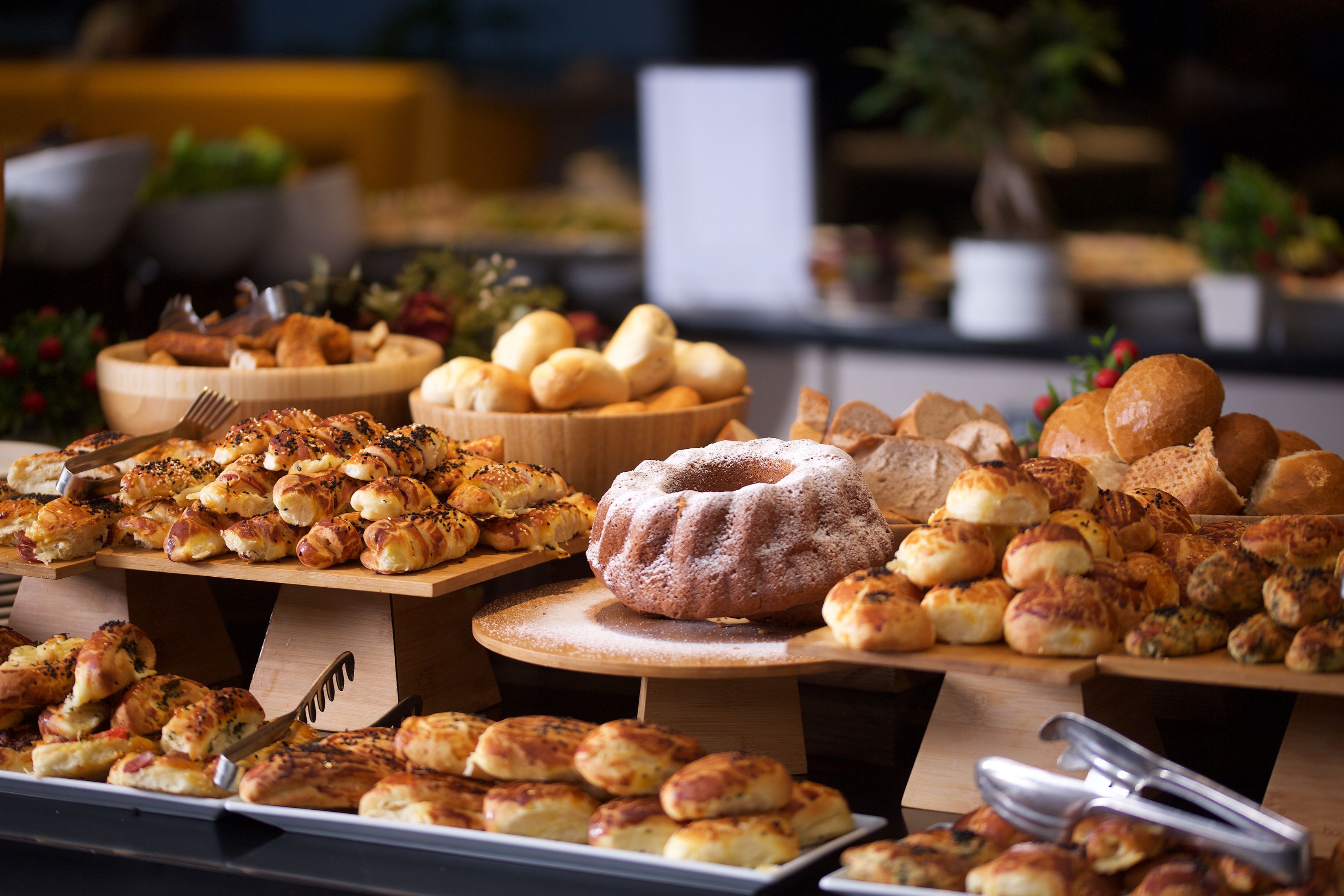 Un bufé con diversas opciones de panadería, incluyendo pasteles y pan, dispuestas sobre tablas de madera.