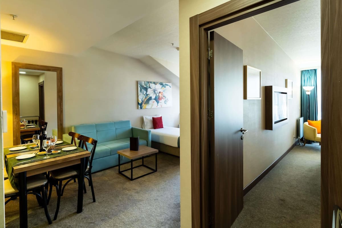 Habitación de hotel con comedor, sofá, una mesita y puerta que da a otra habitación.